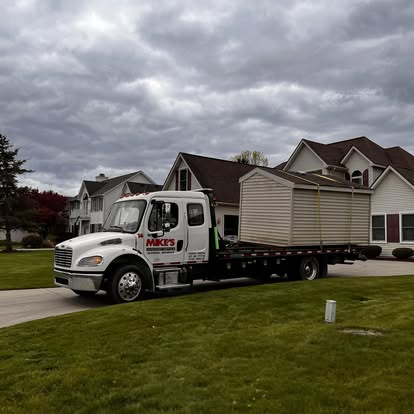 Mike's medium-duty flatbed hauling a shed on a residential street