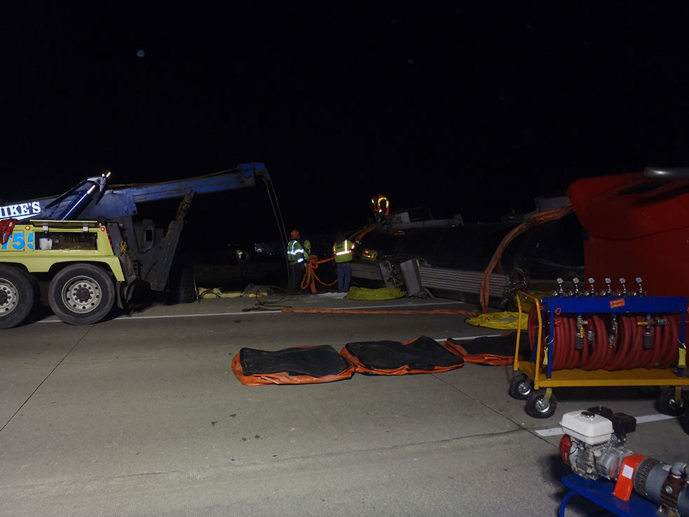 Night highway recovery with a Mike's Wrecker truck on scene and recovery gear laid out across the road