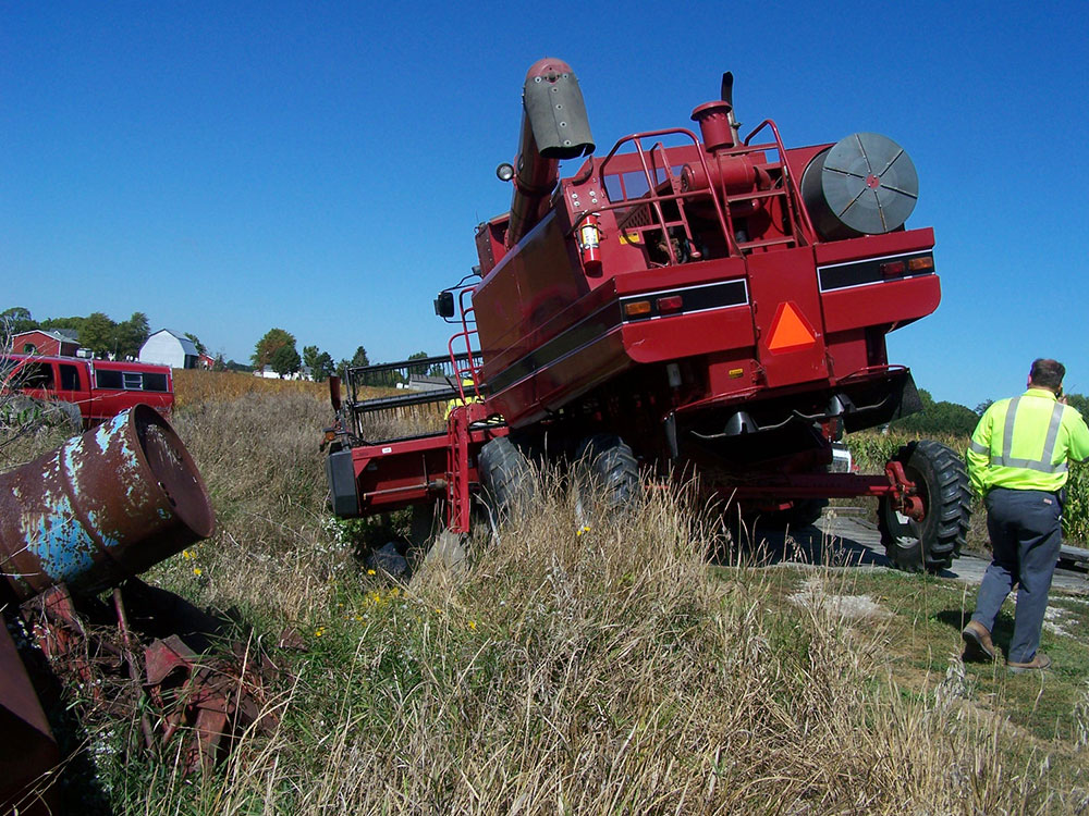 Red combine harvester tilted on a grassy embankment during a farm equipment recovery
