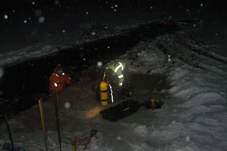 Crew in dry suits working on the ice at night during a snowfall